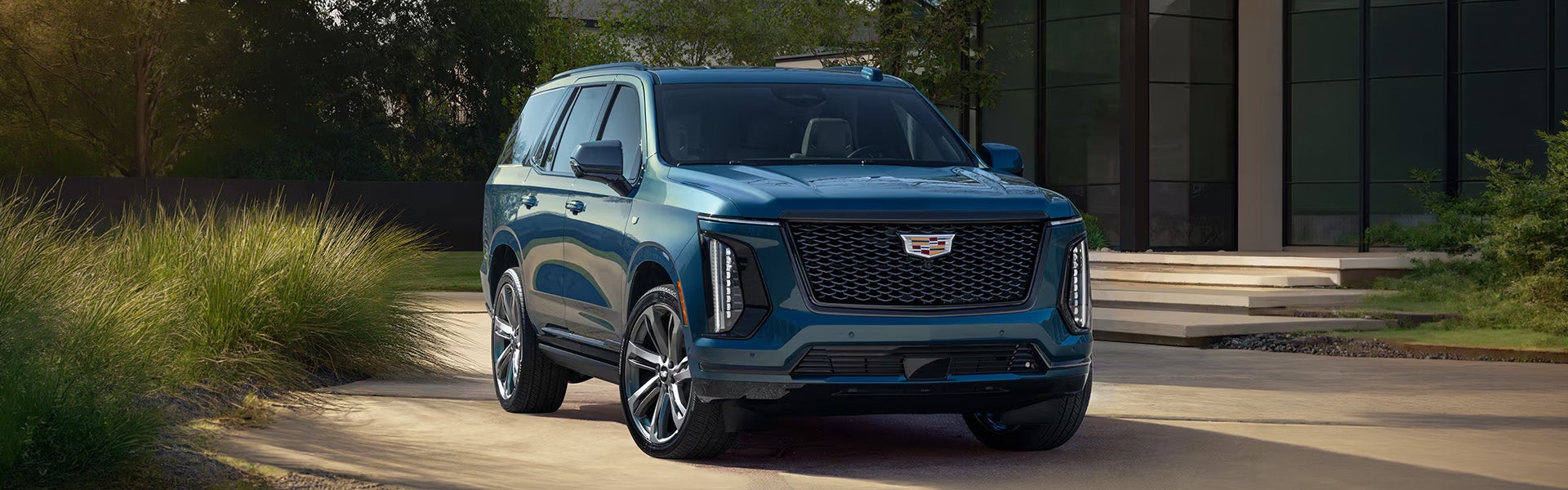 Front view of a teal blue Cadillac Escalade parked on a paved driveway.